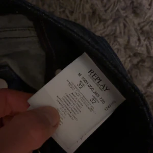 Replay jeans i mörkblå denim - Säljer ett par Replay jeans i mörkblå tvätt med klassisk femficksdesign och smal passform. Jeansen har snygga slitningar och detaljerade sömmar, samt dragkedja och knappar framtill. Perfekta för dig som gillar stilrena och moderna jeans.