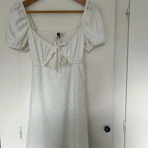 Vit klänning med broderade detaljer och puffärmar - Superfin vit klänning från H&M med broderade blommor och puffiga kortärmar. Klänningen har knytning framtill och en söt, romantisk känsla. Perfekt för sommarens alla tillfällen!