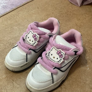 Hello Kitty sneakers med fluffiga rosa snören - Säljer ett par vita sneakers med rosa detaljer och fluffiga rosa snören. Skorna har Hello Kitty-motiv både på plösen och innersulan. Perfekta för dig som älskar söta och unika skor! OBS! SKORNA ÄR REDAN TVÄTTADE (bilderna är gamla och skickar gärna nya bilder privat!)  använda ca 2 ggr.