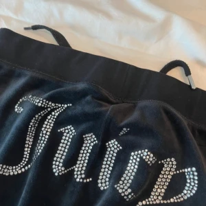 Svarta velourbyxor från Juicy Couture - Säljer ett par klassiska svarta velourbyxor från Juicy Couture med strassdetaljer på baksidan och broderad logga framtill. Byxorna har dragsko i midjan och stora fickor fram. 