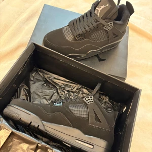 Jordan 4 - Säljer ett par helsvarta Nike Air Jordans med klassisk siluett och detaljer i mesh och läder. Skorna har snörning och platt sula, perfekt för dig som gillar streetwear och vill ha en stilren look.