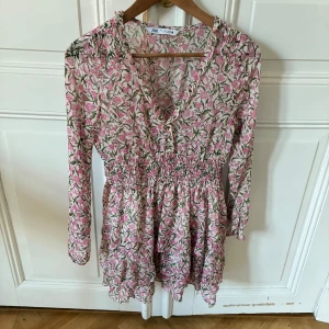 Blommig kortklänning från Zara - Supersöt kortklänning från Zara med rosa och grönt blommönster. Klänningen har lång ärm, smock i midjan och knytning vid halsen. Hör av dig vid frågor💞💞