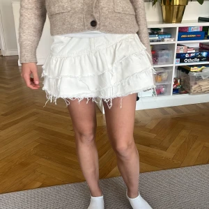 Vit volangkjol från Perfect Jeans - Supersöt vit jeanskjol med flera volanger och råa kanter från Gina tricot. Kjolen har klassisk femficksdesign och knapp framtill. Perfekt för dig som vill ha en trendig och lekfull look. Pris kan diskuteras!❤️