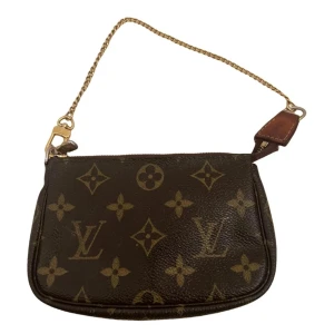 Louis Vuitton Monogram Mini Pochette - Säljer en klassisk Louis Vuitton Mini Pochette med monogrammönster och guldfärgad kedja. Väskan har dragkedja och detaljer i brunt skinn. Perfekt som accessoar till din outfit.