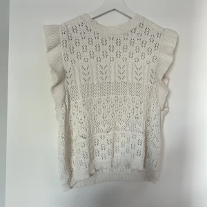 Vit stickad topp med volang från ONLY - Säljer en söt vit stickad topp från ONLY med volangdetaljer längs axlarna. Toppen har ett hålmönster och ribbad kant vid hals och nederdel.  Ganska liten i storleken så skulle mer säga att det är en M/L än en XL. Säljes då den inte kommer till användning längre. 