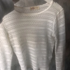 Vit spetströja från Hollister - Säljer en vit långärmad tröja från Hollister med spetsstickat mönster. Perfekt att ha över en snygg bralett eller linne!