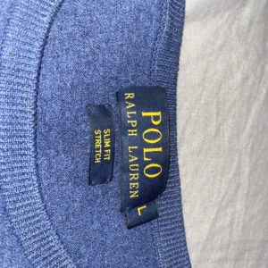 Blå slim fit tröja från Polo Ralph Lauren - Säljer en blå slim fit tröja från Polo Ralph Lauren med stretch. Tröjan har rund halsringning, långa ärmar och en liten röd broderad logga på bröstet. Perfekt för dig som gillar klassisk och stilren design.