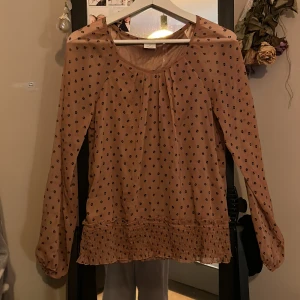 Smutsrosa blus med prickigt mönster - Säljer en smuts rosa blus med svarta prickar och långa ärmar. Blusen har en lös passform och ribbad nedtill. Perfekt för dig som gillar en luftig och söt stil.
