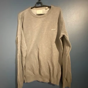 Grå stickad tröja från GANT - Säljer en stilren grå stickad tröja från GANT i storlek S. Tröjan har rund halsringning och långa ärmar, perfekt för lager-på-lager. Diskret GANT-logga broderad på bröstet. Passar även xs.