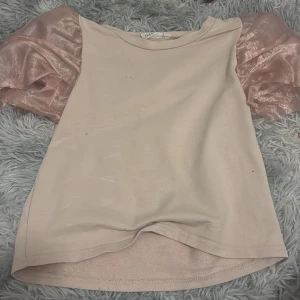 Ljusrosa topp med puffärmar från KappAhl - Supersöt ljusrosa topp från KappAhl med glansiga puffärmar i transparent material. Perfekt för dig som vill ha något unikt och trendigt. Toppen har rund halsringning och korta ärmar med volym.