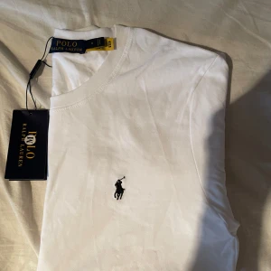 Vit t-shirt från Polo Ralph Lauren - Storlek M passar s också , Helt ny aldrig använd med tags. Säljer en klassisk vit t-shirt från Polo Ralph Lauren med broderad svart logga på bröstet. T-shirten har rund halsringning och är tillverkad i mjuk bomull. Perfekt basplagg för garderoben.