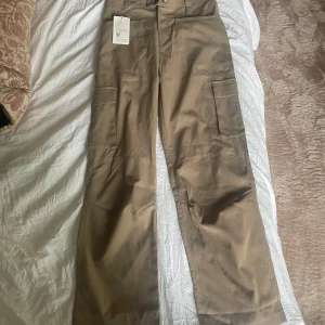 Beige Bruna cargobyxor - Säljer ett par beiga cargopants från YAZE med raka ben och stora fickor på sidorna. Byxorna har hög midja och stängs med dragkedja och knapp. Aldrig använda.