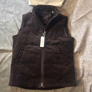 Svart manchesterväst från John Henric - Säljer en brun väst i manchestertyg från John Henric. Västen har hög krage, två framfickor och stängs med dragkedja. Perfekt för lager-på-lager och stilren look. Har tyvärr inte kvar tag och påse.