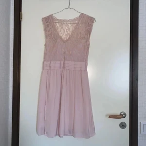 Ljusrosa spetsklänning - Söt ljusrosa klänning med spets upptill och v-ringad hals. Bred midjedetalj och lätt utställd kjol i chiffongliknande material. Perfekt för vårens och sommarens tillfällen. Ny pris var 450kr. 