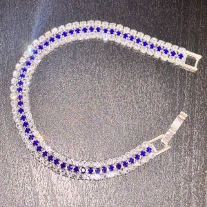 Diamant armband med blå stenar - Säljer ett glittrigt armband i silverfärg med två rader klara stenar och en rad blå stenar i mitten. Armbandet har ett klassiskt spänne och passar perfekt för kombination med klänning eller något finare.