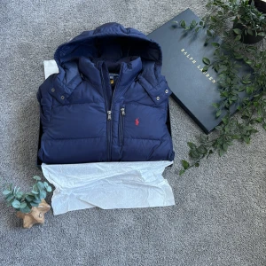 Mörkblå dunjacka med huva från Ralph Lauren - | MARINBLÅ DUNJACKA FRÅN POLO RALPH LAUREN TILL SÄLJES! | 10-12 / 140-150 | Jackan är nästintill nyskick förutom ett hål vid en av sido fickerna | ALLT OG MEDKOMMER! | Hör av dig vid minsta lilla fråga! | jackan är använd en vinter | Rimligt pris som ej är hugget i sten |