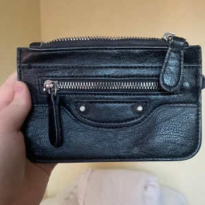Svart plånbok med dragkedja - Säljer en svart plånbok i skinn med silverfärgade detaljer och dragkedja.