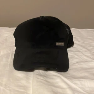 Svart keps från Maggiore - Snygg svart keps från Maggiore med mesh-detaljer på baksidan för extra ventilation. Kepsen har en justerbar rem för perfekt passform och en metallplatta med varumärkeslogga framtill. Spännet är dock lite trasig som man ser på bild 5 så priset kan diskuteras.