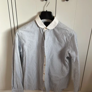 Faconnable skjorta - Snygg skjorta från Faconnable i blåvitt randigt mönster och med kontrasterande vit krage. Klassisk passform med långa ärmar och knappar framtill. Perfekt för en stilren look.