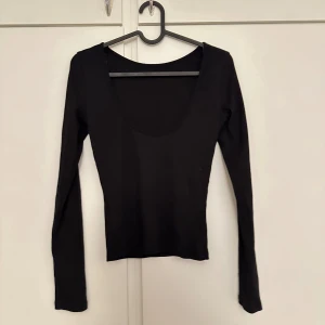 Svart långärmad topp med djup ringning baktill - En stilren svart långärmad topp med djup rundad ringning baktill. Toppen har en tight passform och är tillverkad i ett stretchigt material som sitter snyggt på kroppen. Perfekt att matcha med jeans eller kjol.