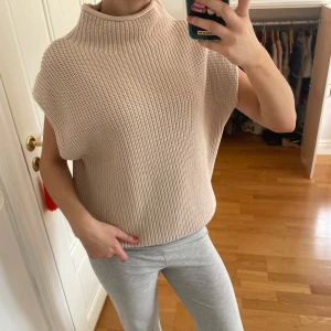 Beige stickad ärmlös tröja - Säljer en beige stickad ärmlös polotröja med bred ribbad struktur. Tröjan har hög krage och avslappnad passform, super skön att allmänt ha i skola/jobb men också mys hemma