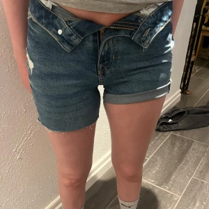 Blå jeansshorts  - Säljer ett par klassiska blå jeansshorts med hög midja och raka ben. Shortsen har upprullade benslut, slitningar och femficksdesign. Perfekta för varma dagar och enkel att matcha med olika toppar. Hör av er vid frågor eller fler bilder.💛