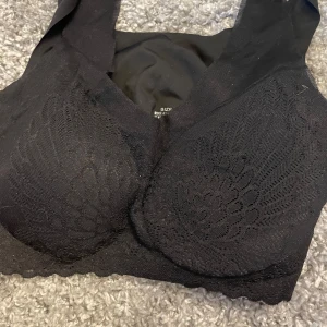 Svart spets bralette - Svart bralette med vacker spetsdetalj framtill. Mjuk och stretchig modell utan byglar, perfekt för en bekväm känsla hela dagen. Bred resår nedtill och breda axelband för extra stöd.