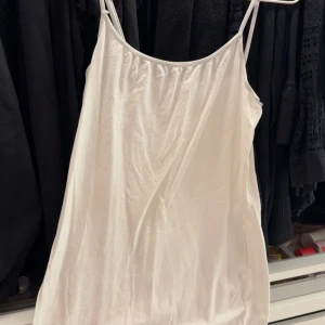 Vit linnetopp med tunna axelband - Säljer en enkel och stilren vit linnetopp med tunna axelband. Perfekt att matcha med jeans eller kjol för en fräsch look. Tunt och lätt material som passar bra till varma dagar.