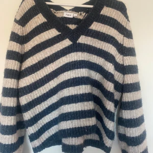 Randig stickad tröja från Saint Tropez - Mysig stickad tröja från Saint Tropez i storlek L. Tröjan har breda marinblå och beige ränder, v-ringad hals och långa ärmar. Perfekt för lager-på-lager och chill dagar. Snygg och avslappnad passform.