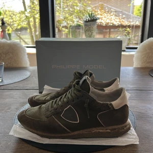 Philippe Model TRPX - Säljer ett par Philippe Model sneakers i grön mocka och cordura med vita detaljer. Skorna har snörning, rund tå och en platt sula med kamouflagemönster. Klassisk Philippe Model-logga på sidan och bekväm innersula. Skick: 7-8/10. Används sparsamt. Har en liten defekt på vänstra skon (se bild 4). Öppen för byten ;) Vid frågor och funderingar så tveka inte att skriva!