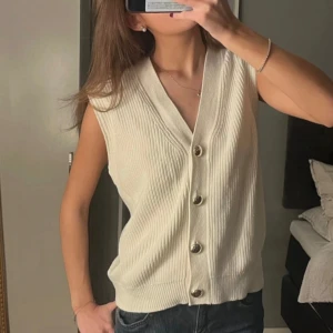 Vit stickad väst/tröja med knappar - Snygg vit väst med v-ringning och stora knappar. Perfekt att styla över en t-shirt eller skjorta. Enkel och stilren design som passar till många outfits.