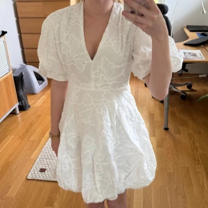 Klänning från Aalborg Modehus - Helt ny superfin vit klänning med puffiga korta ärmar och v-ringning. Klänningen har ett broderat blommigt mönster och ballongformad kjol. Perfekt för sommarens tillfällen och student. Säljs då jag beställde två olika storlekar och den här är för stor. Klänningen är i storlek S. 