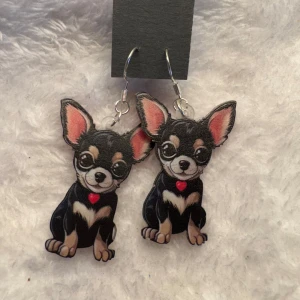 Chihuahua örhängen med hjärtdetalj - Säljer ett par unika örhängen med söta chihuahua-motiv. Örhängena har svarta, vita och rosa färger samt en liten röd hjärtdetalj. Perfekt accessoar för hundälskare som vill sticka ut! Krokarna är i sterling silver