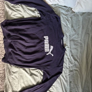 Mörkblå sweatshirt från Puma - Mörkblå sweatshirt från Puma med klassisk logga i vitt framtill. Tröjan har rund halsringning och långa ärmar. Perfekt för en sportig och avslappnad stil.