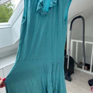Turkos klänning med volang från Aery Bet - Säljer en turkos klänning från Aery Bet i storlek XS. Klänningen har volangdetalj vid halsen och är ärmlös. Perfekt för varmare dagar och har en mjuk, lätt känsla.
