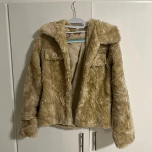 Beige pälsjacka från Colloseum - Säljer en fluffig beige pälsjacka från Colloseum med stora slag och två bröstfickor med knappar. Jackan är helfodrad och har lång ärm, perfekt för kyligare dagar. Supermjuk och trendig modell som ger en lyxig känsla. Den har ingenting att dra upp dragkedjan med.