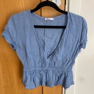 Blå croppad blus från Subdued, stl M - Säljer en ljusblå croppad blus från Subdued med korta puffärmar och djup v-ringning. Blusen har volang nertill och är tillverkad i ett tunt linnematerial, perfekt för varmare dagar.