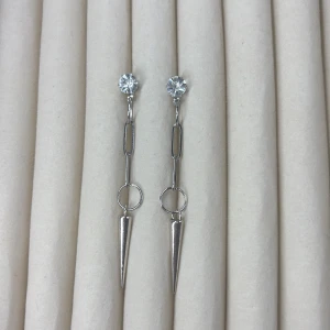 Silverfärgade örhängen med kedja och spetsig detalj - Säljer ett par trendiga silverfärgade örhängen med glittrande sten upptill, kedjelänk i mitten och en lång spetsig hängande detalj. Perfekta för dig som gillar en edgy och modern stil.