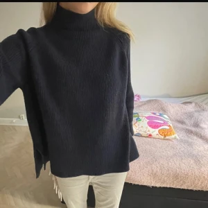 Mörkblå stickad polotröja - Säljer en mörkblå stickad polotröja med hög krage. Tröjan har lång ärm och är i en lös passform, perfekt för kyligare dagar. Enkel och stilren design som passar till mycket.