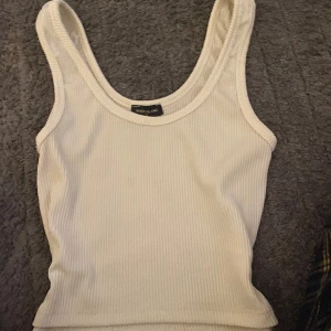 Vit ribbad linnetopp - Säljer en enkel och stilren vit ribbad linnetopp med breda axelband. Perfekt att matcha med jeans eller kjol för en avslappnad look.