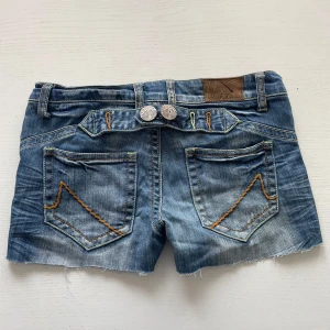 Blå jeansshorts  - Snygga blå jeansshorts med fransig kant och dekorativa sömmar i orange på bakfickorna. Shorts med dubbla knappar bak. Perfekta för varma dagar. Skriv till mig om du har frågor🌸
