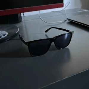 Svarta solglasögon från Tom Ford - Stilrena svarta solglasögon från Tom Ford med klassisk wayfarer-form. Bågarna är i svart plast med diskret logga på sidan. Perfekta för dig som vill ha en tidlös och snygg accessoar till sommaren. Nypris 3 800kr, inga defekter alls.
