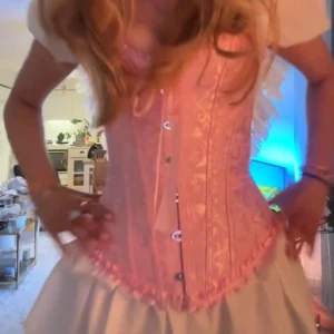 Rosa korsett med spetsdetaljer - INTRESSEKOLL - Säljer en ljusrosa korsett med dekorativa spetsdetaljer och mönster. Korsetten har knäppning framtill och fina sömmar som ger en klassisk siluett. Perfekt för dig som vill ha något unikt och romantiskt.