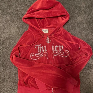 Juicy Couture tröja  - Juicy Couture hoodie i röd velour med glittrande stenar som bildar texten 'Juicy' på bröstet. Tröjan har dragkedja och huva. Perfekt för en trendig och bekväm look. Inga defekter.