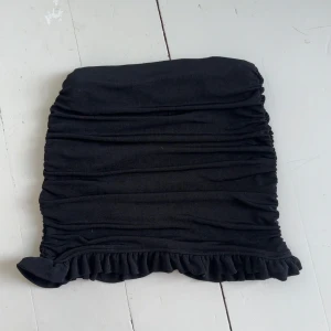 Svart tight minikjol med volang - Svart tight minikjol med rynkade detaljer och volang längst ner. Kjolen har en enkel design som ger en cool och trendig look. Använt få tal gånger.