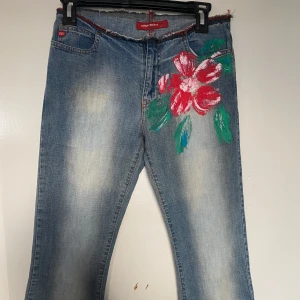 Miss Sixty jeans med blommotiv  - Unika blå jeansbyxor från Miss Sixty med handmålat  blommotiv på framsidan. Byxorna är i utsvängd modell 🌺.