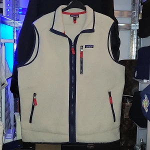Patagonia väst  - Säljer en beige fleeceväst från Patagonia med marinblå detaljer och röda dragkedjor. Västen har tre fickor med dragkedja och klassisk ståkrage. Perfekt för lager-på-lager och outdoor-stil. Typ helt ny asså använts max 10 gånger, köpt i Uppsala på naturkompaniet för 1400, ksk 4-5 månader sen. Har påsen och taggen kvar men inte kvitto tyvärr. Den är XL fast skulle säga mera som L. Den har inga fläckar eller defekter nånstans som man ser på bilderna. Riktigt Nice väst.