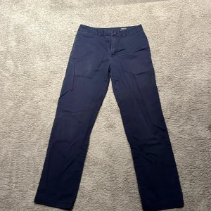 Mörkblå chinos från Polo Ralph Lauren - Snygga mörkblå chinos från Polo Ralph Lauren med klassisk rak passform. Byxorna har två bakfickor med knapp och en röd broderad logga ovanför ena fickan. Nypris ca 1200. Perfekta för en stilren look.