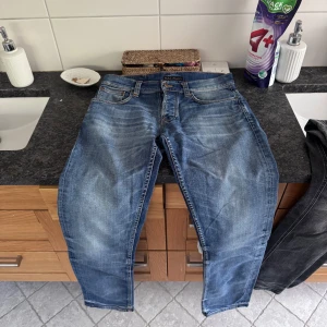 Nudie jeans - Klassiska blå jeans från nudie med fem fickor och dragkedja. Jeansen har en normal passform och raka ben, med snygga slitningar och tvättade detaljer för en avslappnad look.