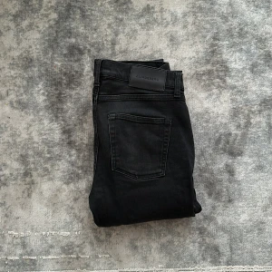 Svarta  jeans från J.Lindeberg - Säljer ett par svarta  jeans från J.Lindeberg. Byxorna har klassisk femficksdesign, normal midja och smal passform hela vägen ner. Perfekta för dig som gillar stilrena och enkla jeans med snygg siluett. Storlek w30 L34